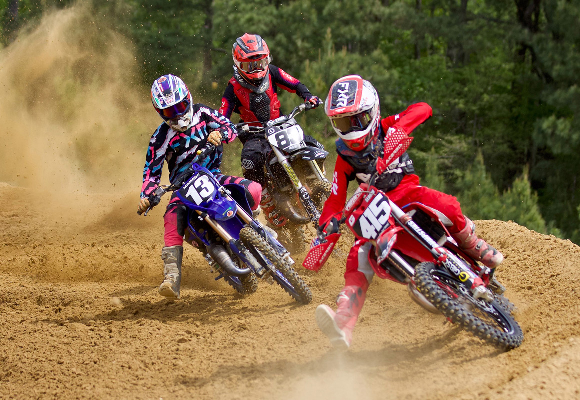 Youth riders racing through a sandy corner at ECMX